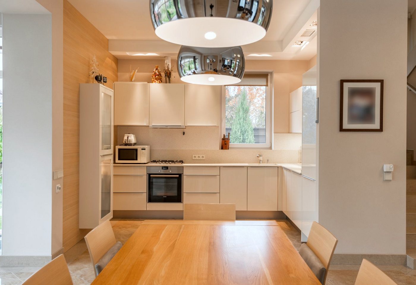 Cream fitted kitchen with white worktops, an oven run and a timber dining table